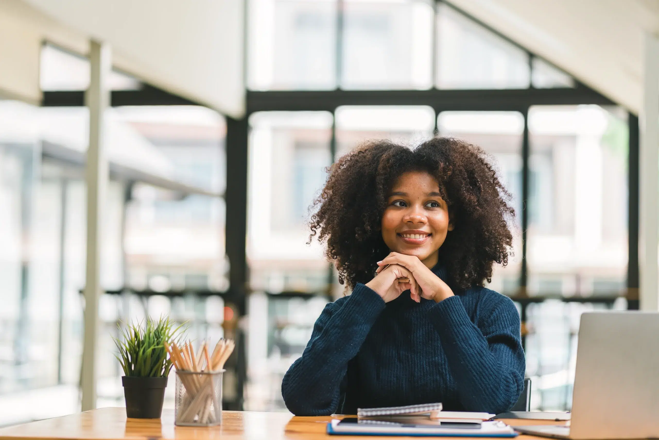 Woman sitting at a desk with a laptop, smiling while reviewing documents—representing staying informed and vigilant about protecting personal information during tax season.